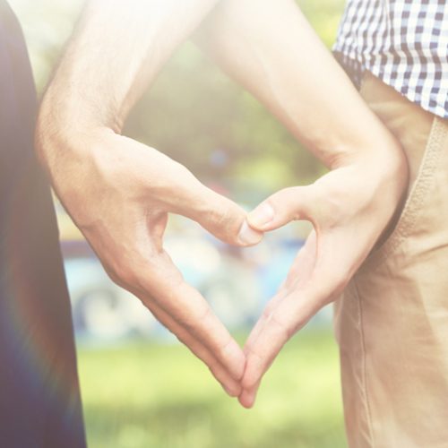 Loving couple holding hands in shape of heart, close-up